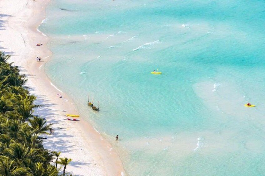 Une plage avec une eau turquoise et limpide, des palmiers, ainsi que quelques personnes et quelques bateaux. 3