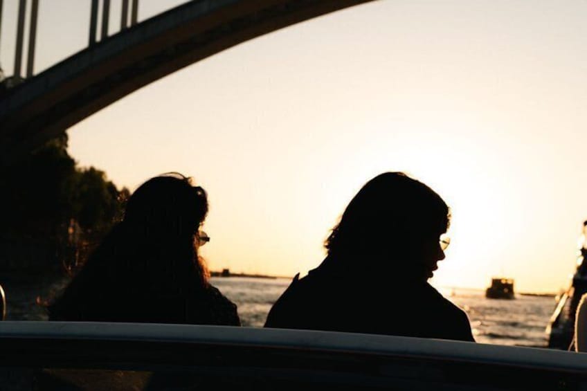 Two people silhouetted against a sunset, with a bridge and water in the background. 5