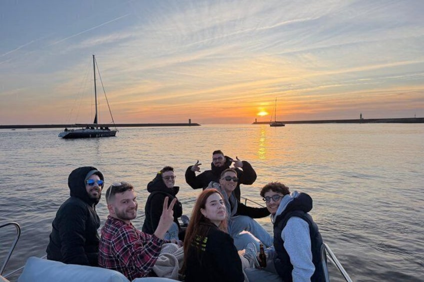 A group of people on a boat at sunset with a sailboat in the background. 4