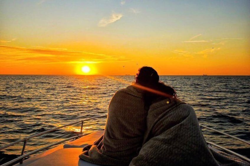 A person sitting on a boat at sunset with the sun visible on the horizon. 1
