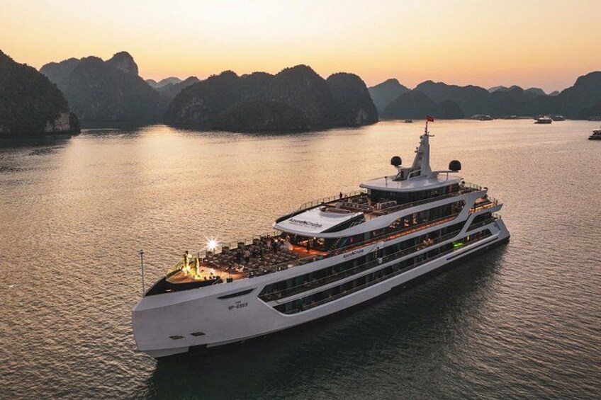 A large, multi-deck cruise ship sailing through a body of water with mountainous terrain in the background. 1