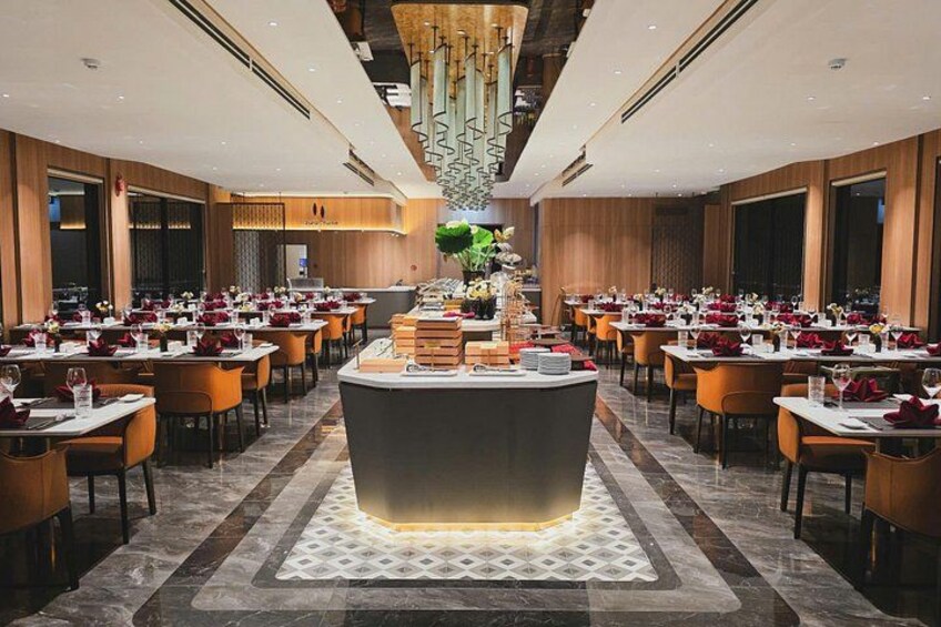 A modern restaurant interior with a central bar, multiple dining tables, and a decorative ceiling light fixture. 2