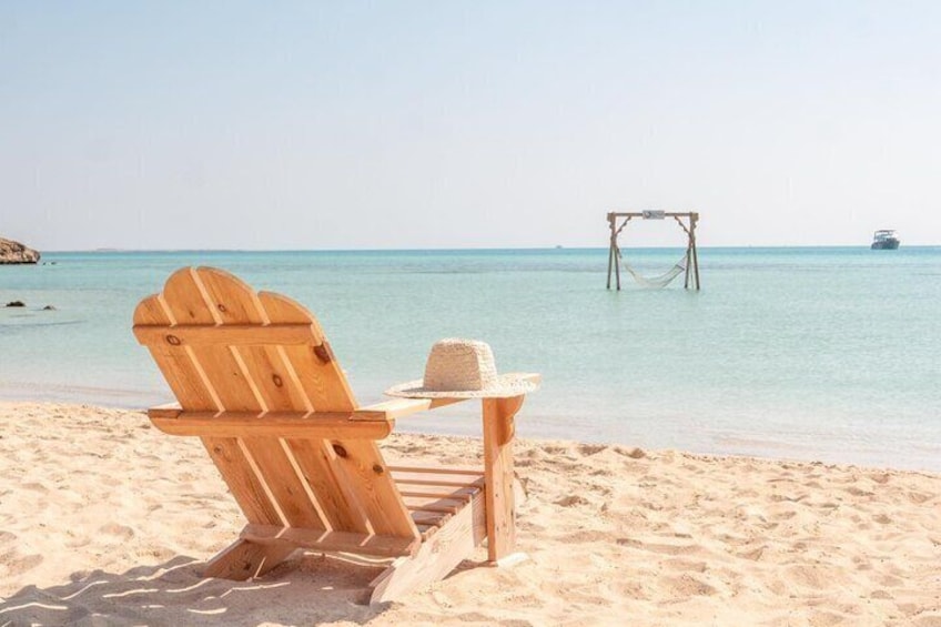 Une chaise en bois et un chapeau sur une plage de sable, avec un hamac en arrière-plan. 3