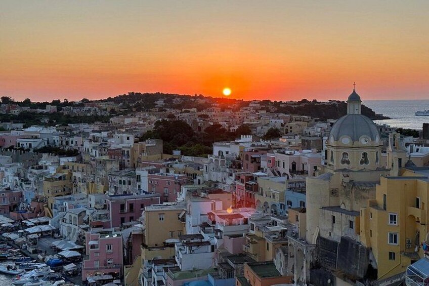 A coastal cityscape at sunset with a prominent church dome, dense urban buildings, and a clear view of the sea. 3