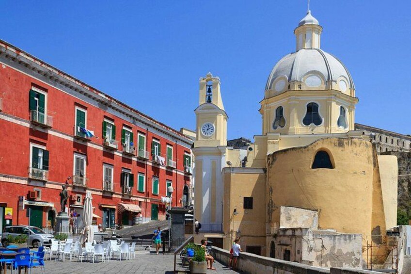A red building with a clock tower, a yellow building with a dome, and outdoor seating. 2