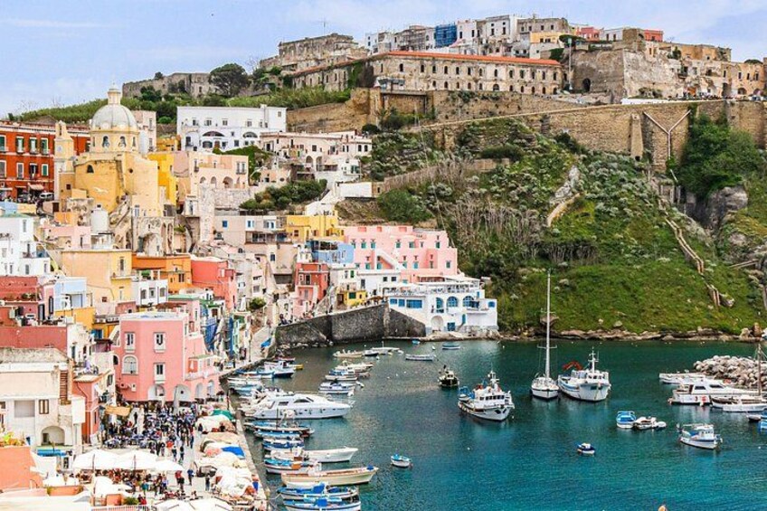 A coastal town with colorful buildings, a harbor with boats, and a historic fort on a hill. 5