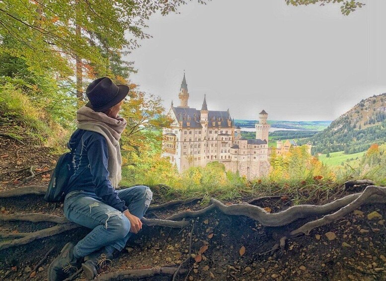 A person sitting on a rock, overlooking a large castle surrounded by trees and hills. 1