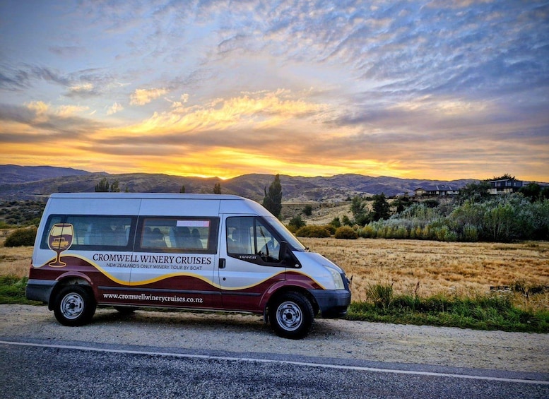 Een busje met de branding 'CROMWELL WINERY CRUISES' geparkeerd aan een weg, met een zonsondergang op de achtergrond. 5