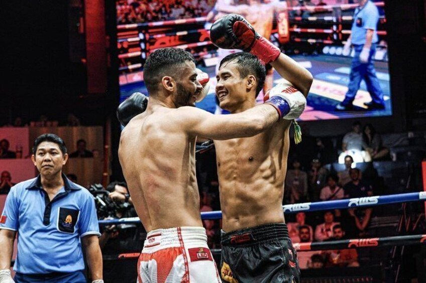 Two boxers in a ring, one with red and white shorts, the other with black shorts, and a referee in blue. 5