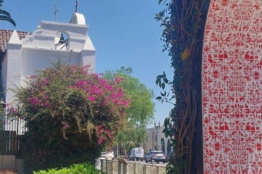 A white church with a bell tower, pink bougainvillea, and a patterned wall. 2
