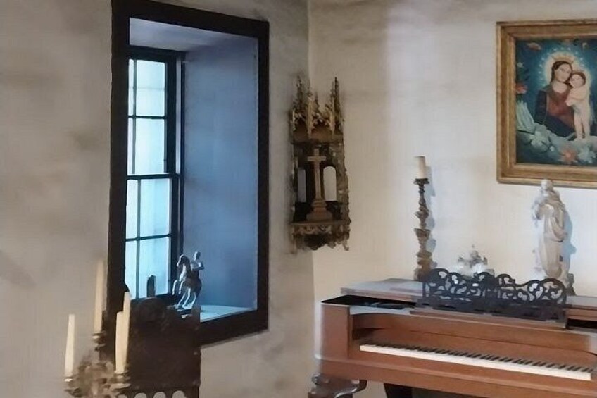 A room with a piano, a mirror, a crucifix, and a religious painting. 3