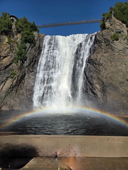 A waterfall with a rainbow, a suspension bridge, and a rocky cliff. 1