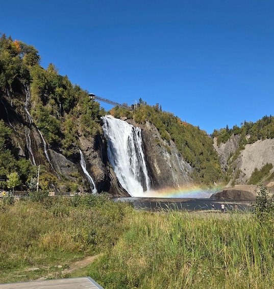 A waterfall with a rainbow, surrounded by greenery and a bridge. 4