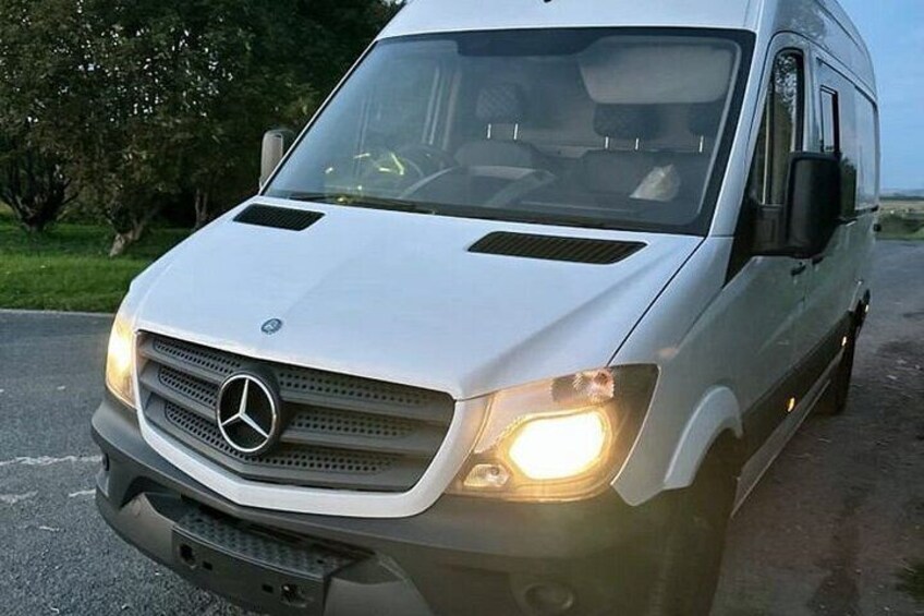 Una furgoneta blanca Mercedes estacionada en una carretera, con vegetación al fondo. 4