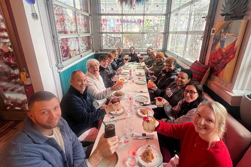 Un gruppo di persone sedute attorno a un lungo tavolo da pranzo in un ristorante con ampie finestre e decorazioni festive. 1