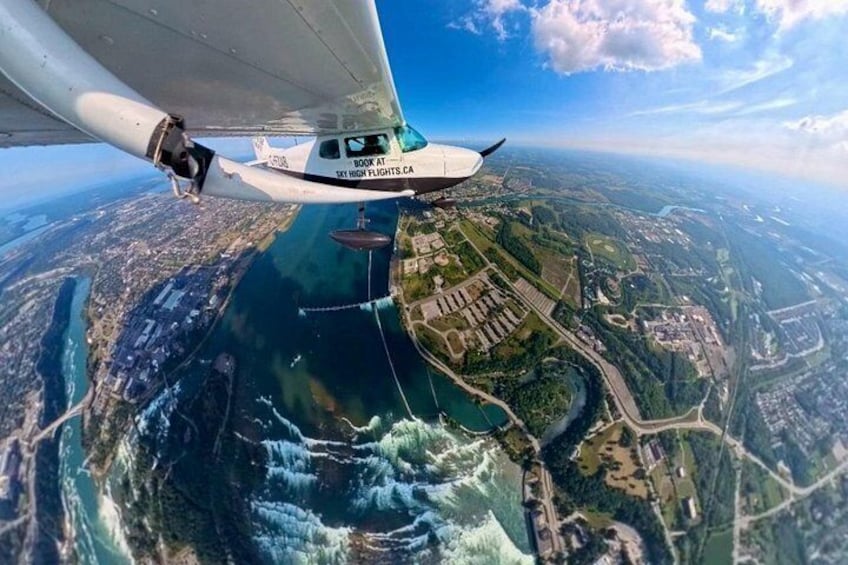 A small aircraft flying over a coastal area with a river and buildings. 3