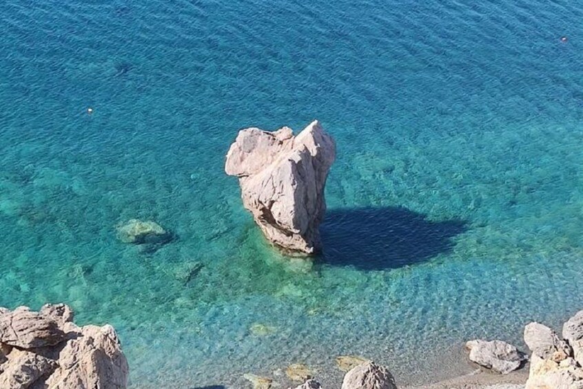 A clear blue sea with a prominent rock formation in the center. 4