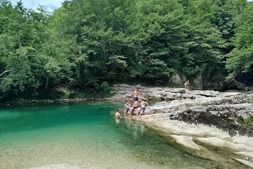 A natural pool surrounded by dense forest, clear water, and rocky terrain. 1