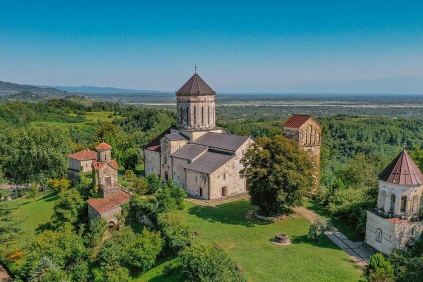 A church complex with multiple buildings, surrounded by lush greenery and a clear sky. 3