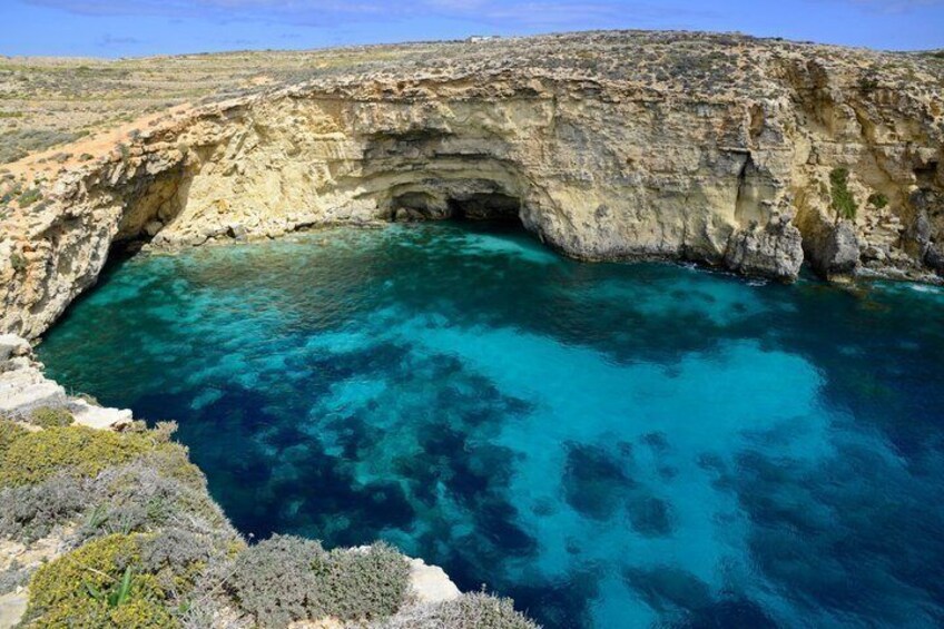 A coastal cliff with a natural cave entrance and clear blue waters. 4