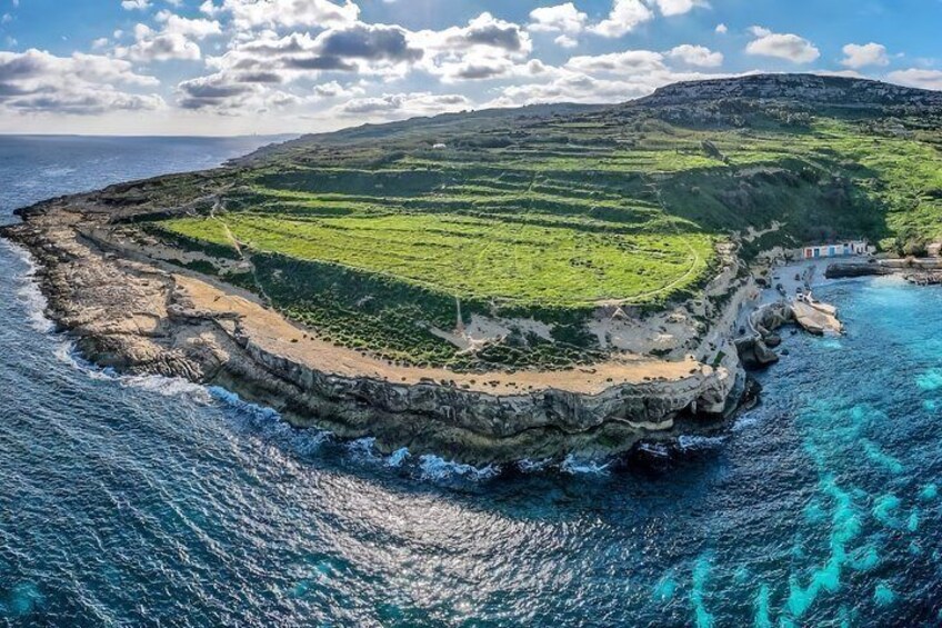A coastal landscape with terraced fields, a rocky shoreline, and a clear blue sea. 1