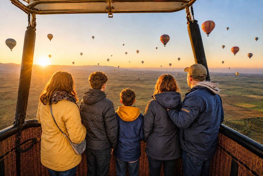 Een gezin van vijf kijkt naar luchtballonnen boven een landschap tijdens de zonsondergang. 1