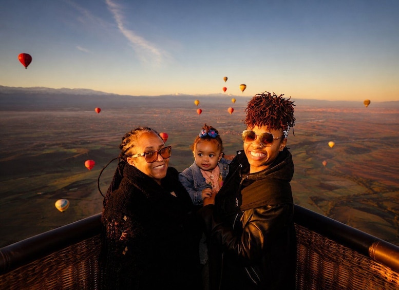 Een groep mensen op een balkon met uitzicht op een landschap met luchtballonnen aan de hemel. 2