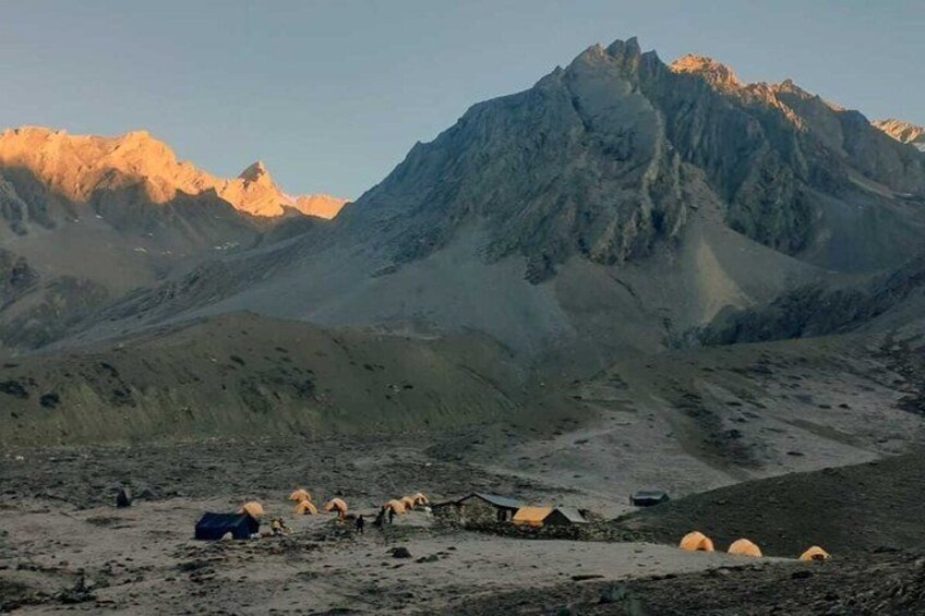 A mountainous landscape with a prominent peak, a few scattered tents, and a clear sky. 2