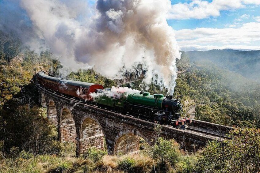 A steam locomotive on a bridge emitting steam. 1