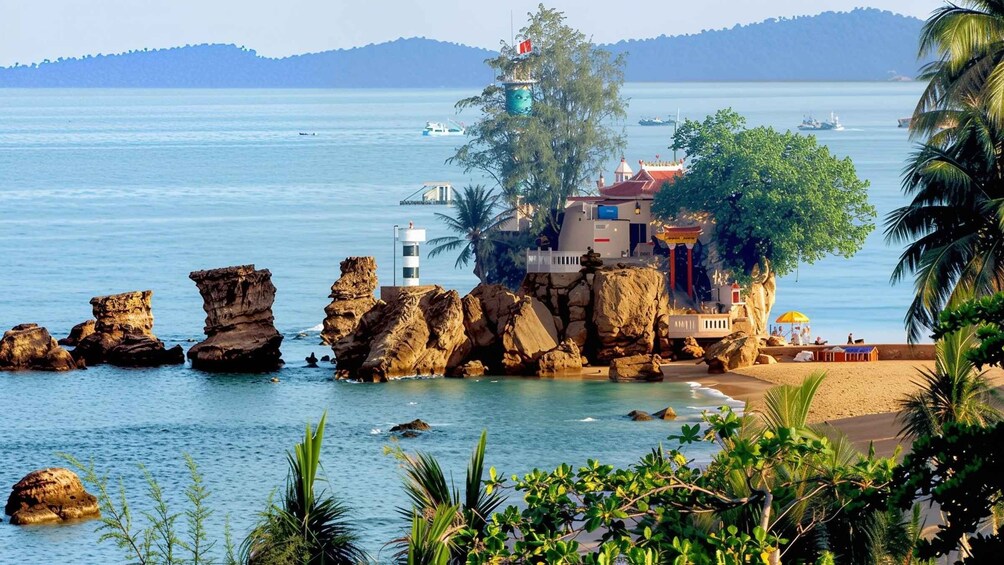 A coastal landscape with rocky formations, a lighthouse, and a beach with palm trees. 5