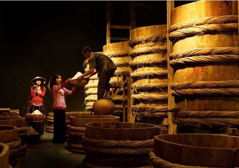 A dimly lit storage area with large wooden barrels and baskets, likely used for storing or aging wine or similar products. 3