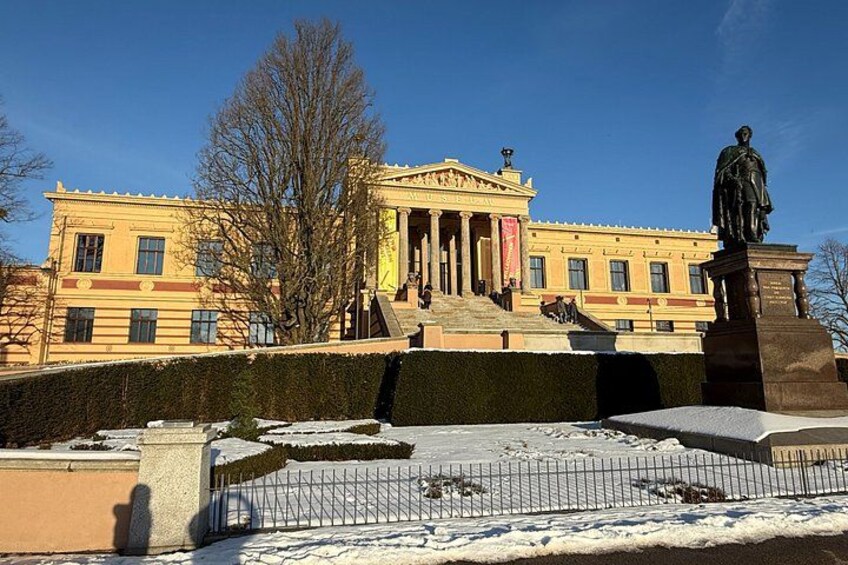 A classical building with columns, a statue, and snow on the ground. 4