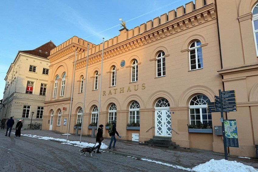 A building with the name 'RATHAUS' on its facade, a street with people walking, and a dog on a leash. 2