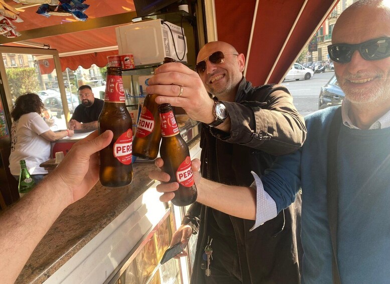People holding bottles of Peroni beer at a street-side stand. 1