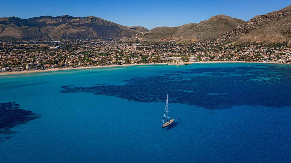 A coastal town with a clear blue sea, a sailboat, and mountains in the background. 5