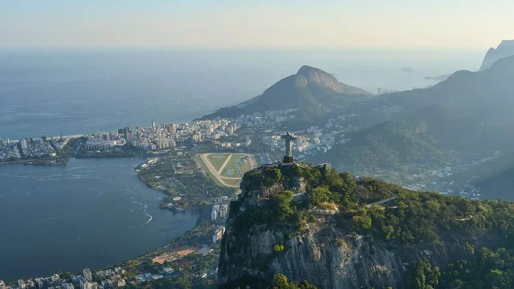 A cityscape with a prominent mountain, a body of water, and a statue on a hill. 5