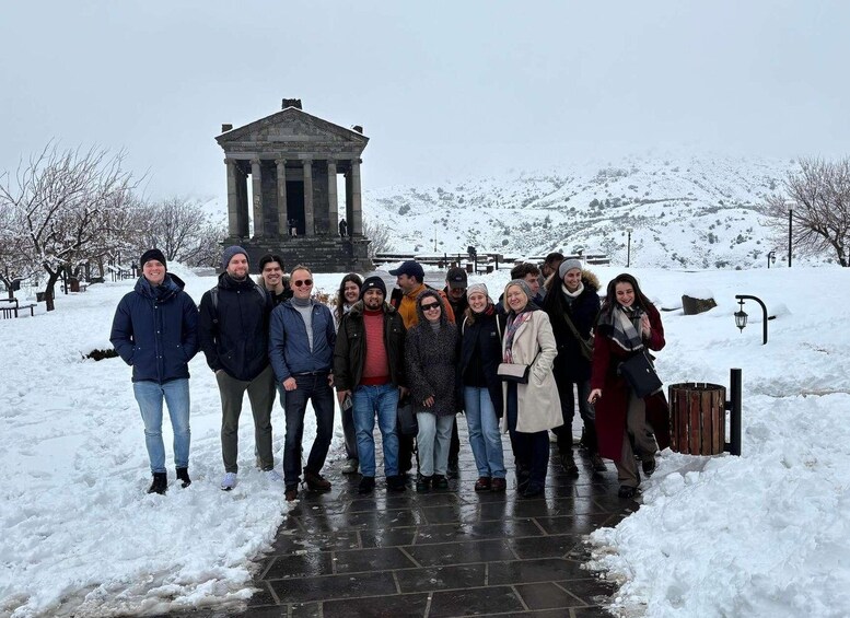 A group of people standing in front of a neoclassical building with columns, surrounded by snow-covered hills. 1