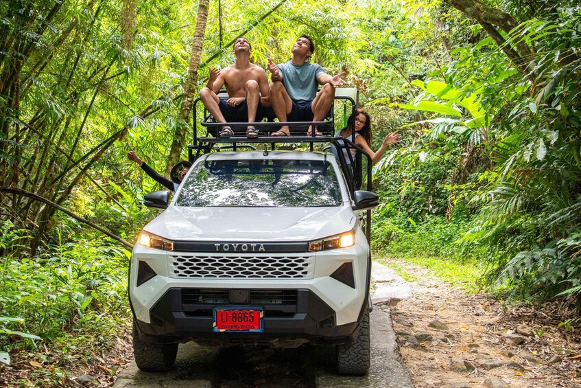 A white Toyota vehicle on a narrow forest trail with dense green foliage on both sides. 2