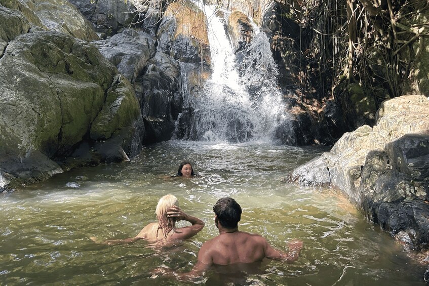 A waterfall in a rocky, forested area with people swimming in the water. 5