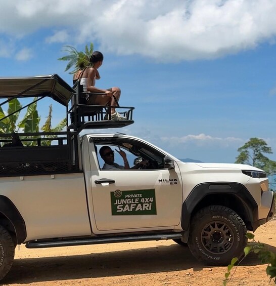 A white off-road vehicle with a person sitting on the roof and another inside the cabin. 2