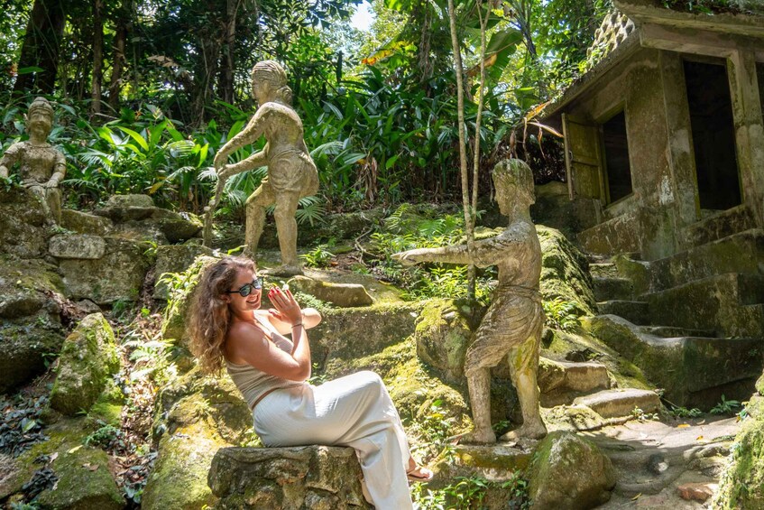 A person taking a photo with stone statues in a lush, tropical garden. 4