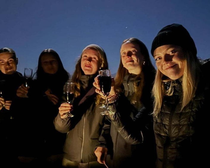 A group of people holding wine glasses, standing outdoors at night. 5