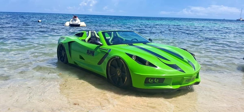 Un coche deportivo verde brillante estacionado en una playa arenosa, con agua azul cristalina y un barco al fondo. 3
