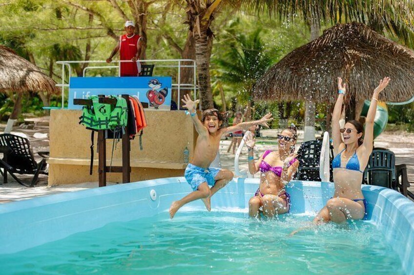 A group of people in a pool with a lifeguard and a thatched roof structure. 3