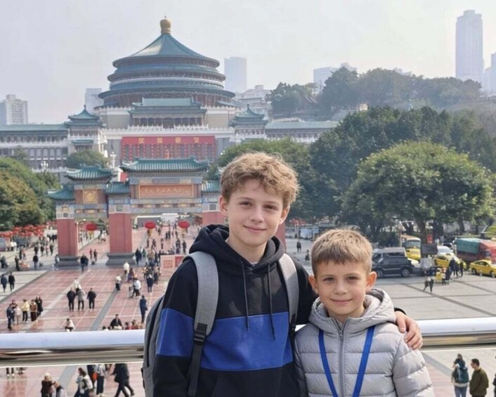 Two individuals in front of a traditional Chinese architectural landmark with a busy street in the background. 4
