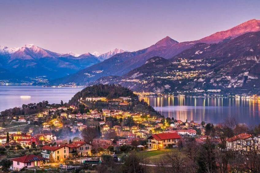 A lakeside town at dusk with illuminated buildings, mountains in the background, and a calm lake. 5