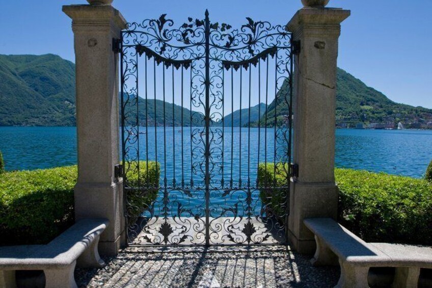 A wrought iron gate leading to a body of water with mountains in the background. 3