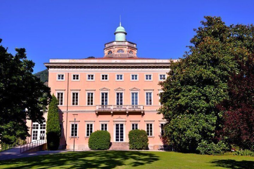 A pink building with a dome and a clock tower, surrounded by trees and a well-maintained lawn. 4