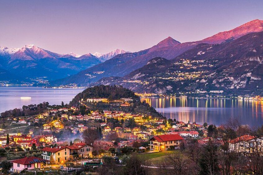A lakeside town with illuminated buildings, a mountain backdrop, and a calm lake. 2