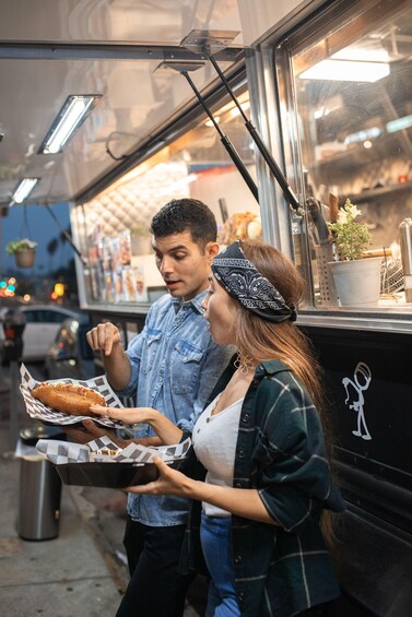 A person holding a tray with a wrapped sandwich and another person standing beside them. 3